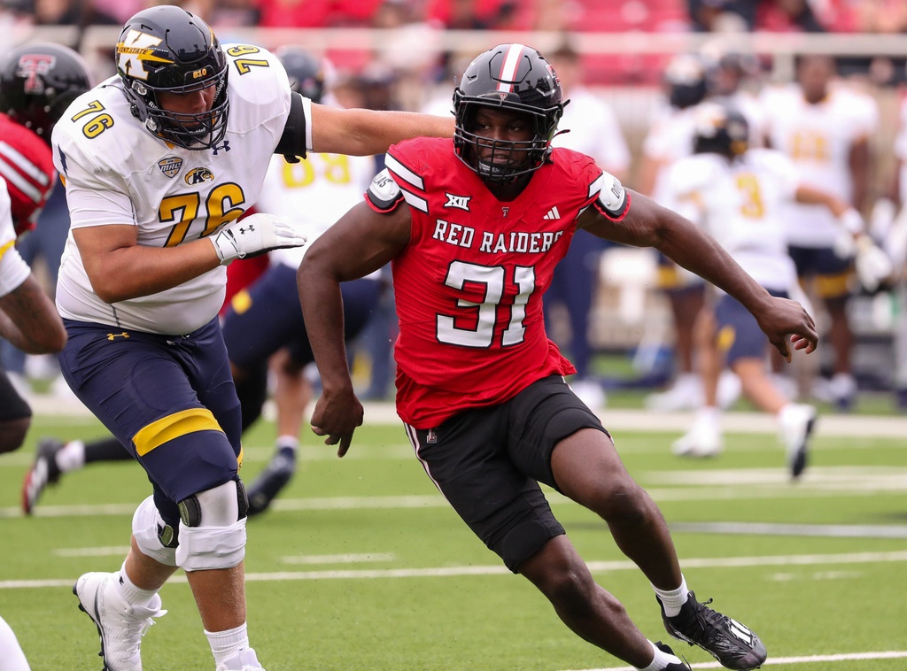 College football action: a Red Raiders player in red jersey #31 runs with the ball as a defender in white and gold (#76) comes in from the left to tackle.